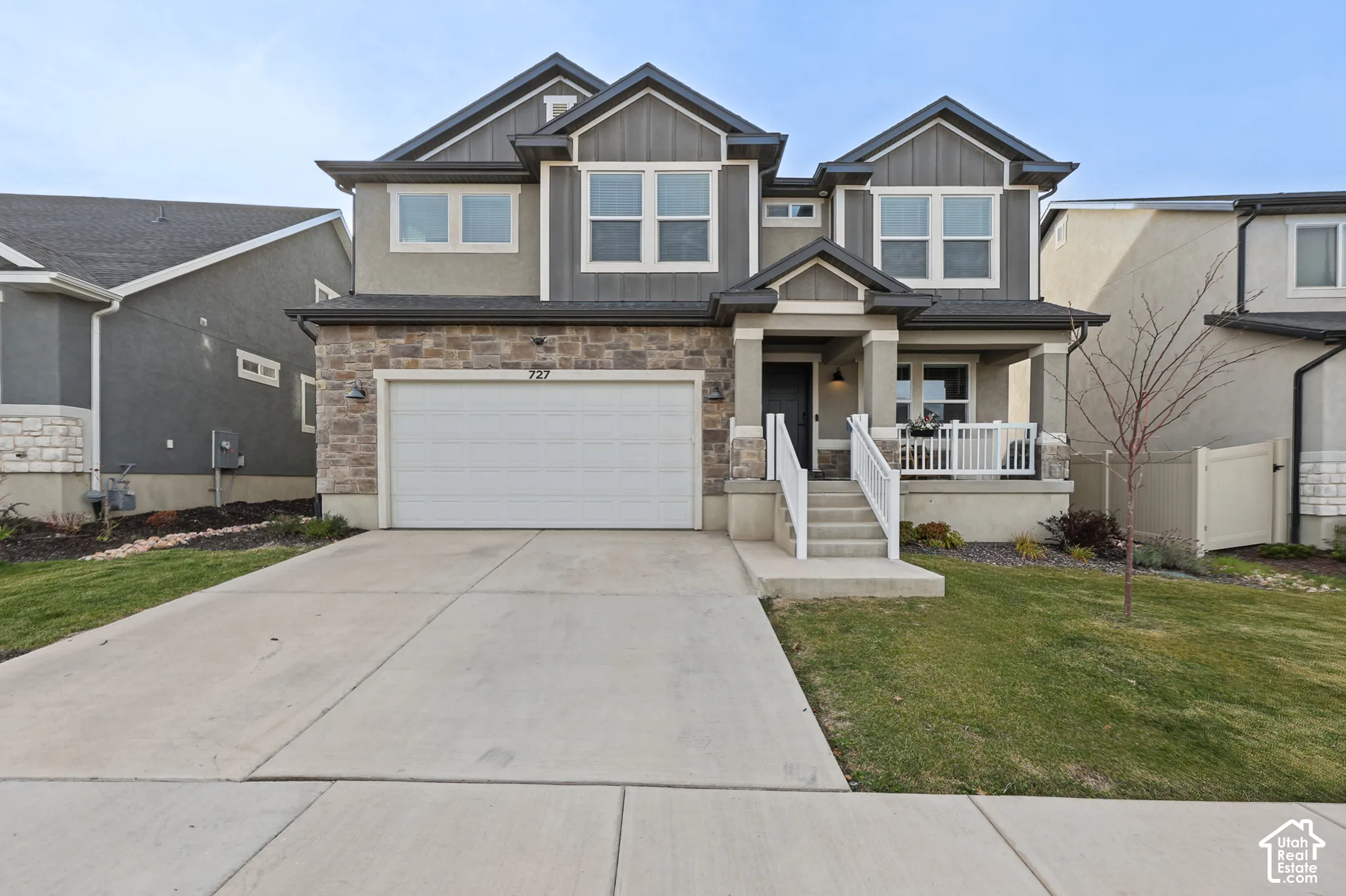 Two-story residence featuring a stone and vertical siding exterior, a covered front porch with white railing, and an attached two-car garage