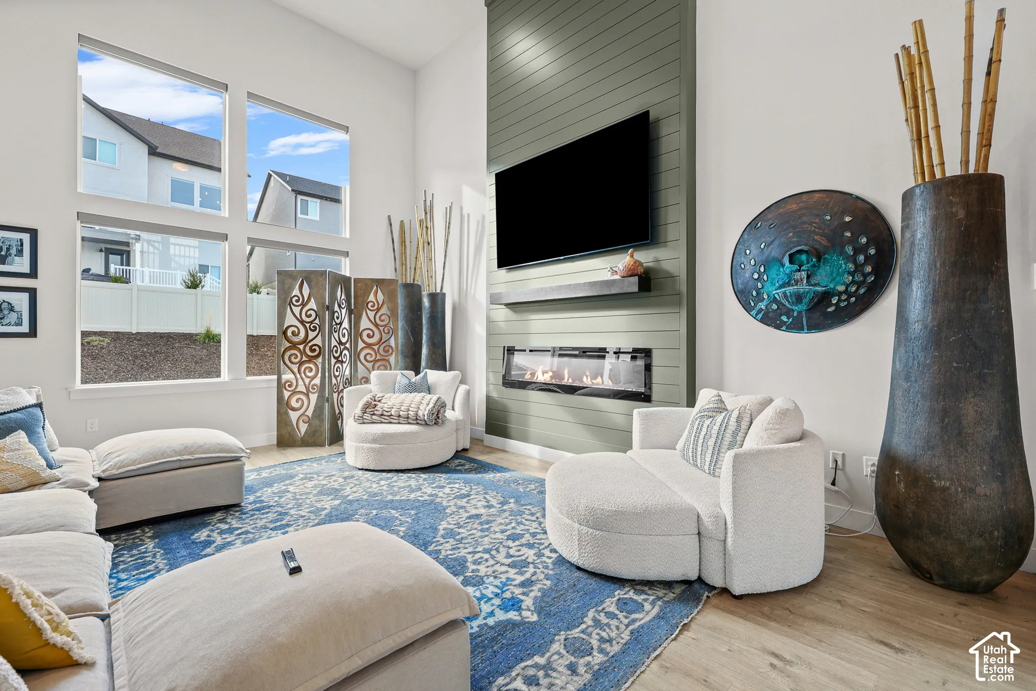 Double-height ceilings, floor-to-ceiling windows, linear electric fireplace, full-height paneled chimney breast, and wood-finish flooring
