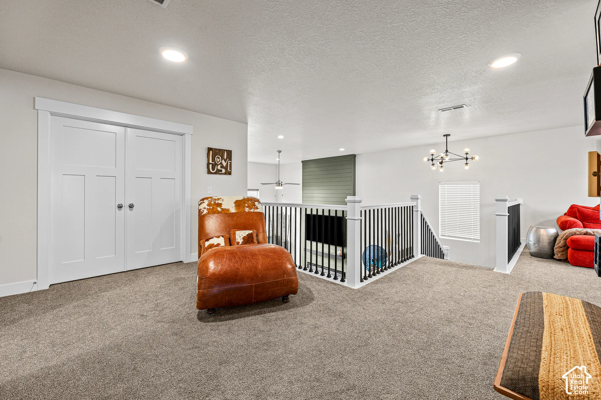 Carpeted open-concept space featuring double-panel interior doors, recessed lighting, a modern multi-arm chandelier, and a decorative railing with vertical balusters