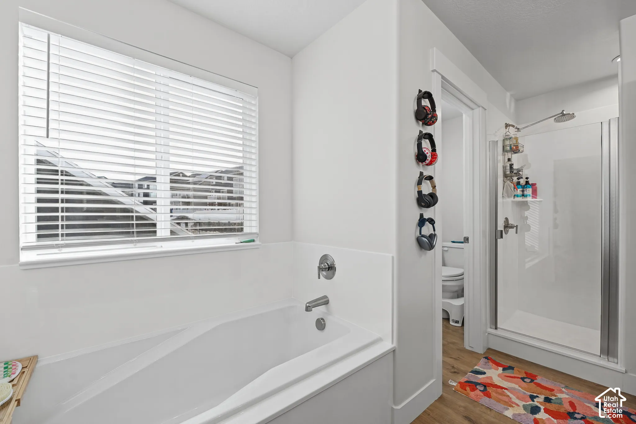 Soaking tub with a tiled surround, wood-finish flooring, and a separate glass-enclosed shower featuring chrome fixtures
