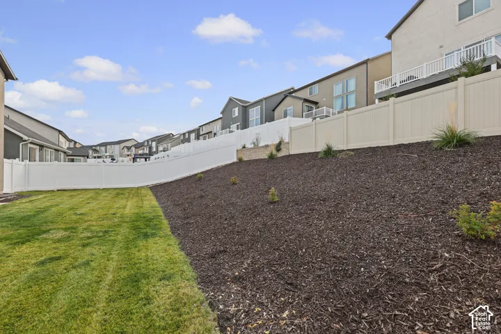 Backyard featuring a grass lawn, sloped landscape with dark mulch, and white vinyl privacy fencing