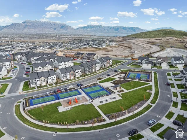 Community park featuring multi-use sports courts, playground equipment, manicured lawn areas, and mountain scenery