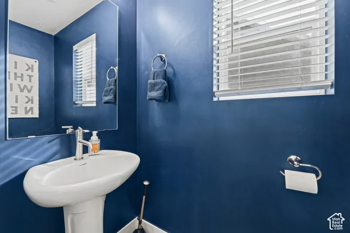 White pedestal sink with a polished chrome faucet, large rectangular wall-mounted mirror, and window with adjustable horizontal blinds