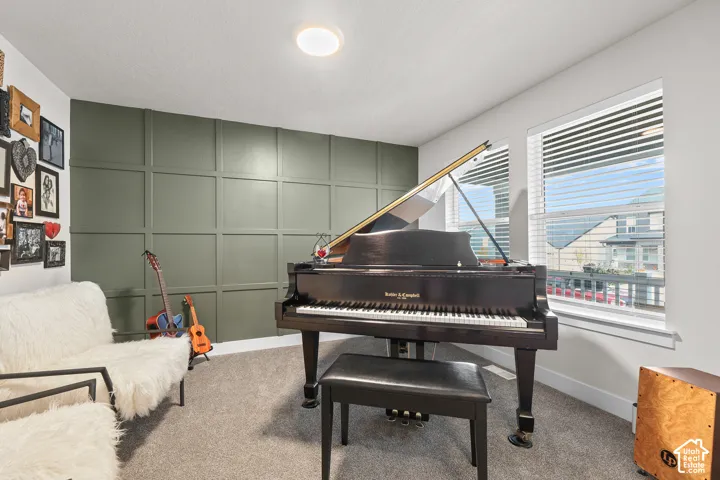 Room featuring an olive green grid-patterned accent wall, wall-to-wall carpeting, and double-pane windows with horizontal blinds