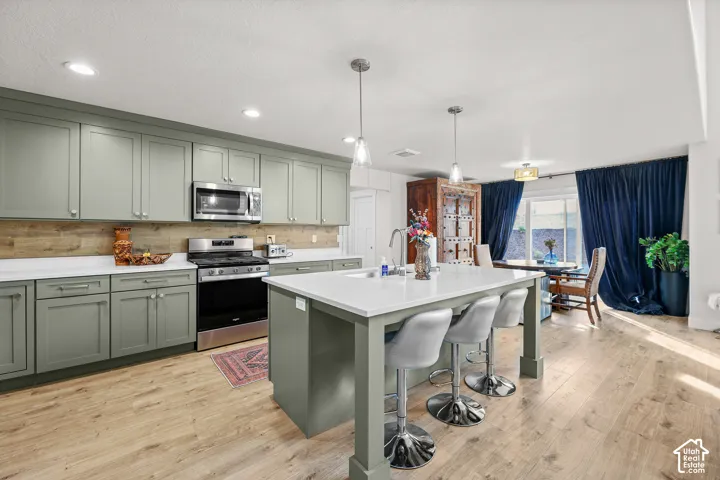 Kitchen featuring sage green cabinetry, white stone-finish countertops, wood-finish flooring, a central island with integrated sink, and recessed lighting