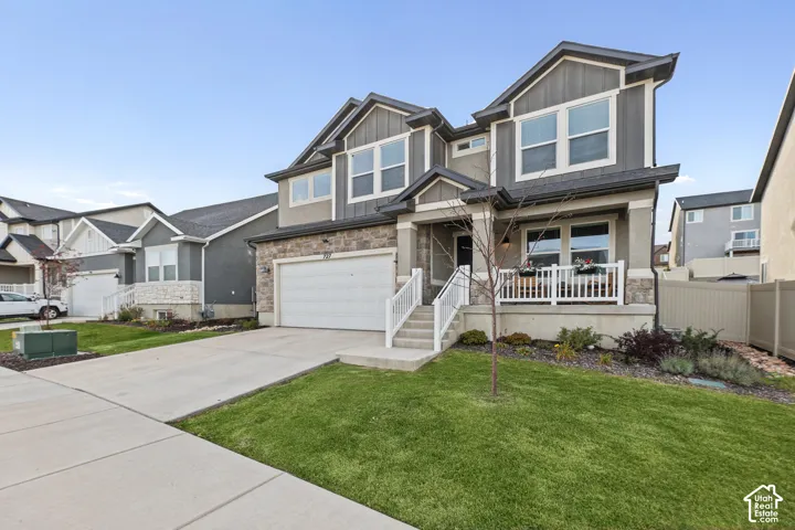Two-story exterior featuring stone veneer accents, vertical siding, a covered front porch with white railing, and an attached two-car garage
