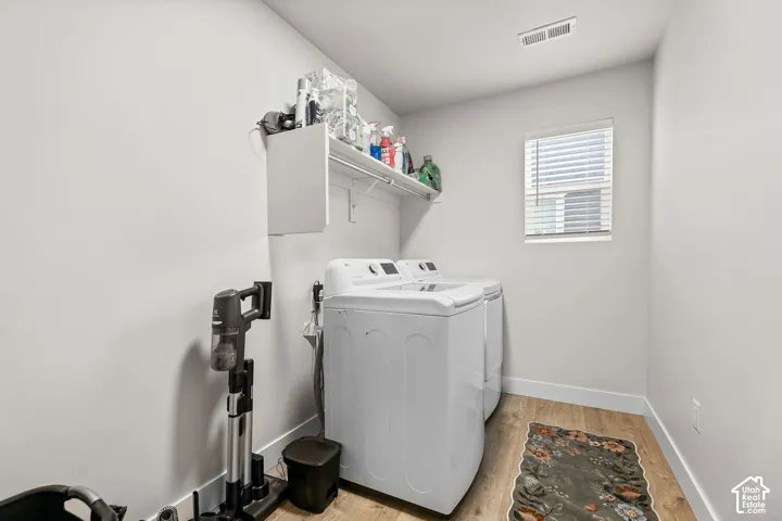 Utility area featuring wood-finish flooring, a wall-mounted white storage shelf, and a window with horizontal blinds