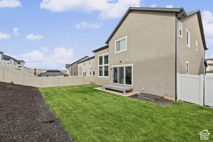Rear exterior featuring stucco siding, multi-pane windows, sliding glass door, a low-profile platform deck, and full vinyl perimeter fencing enclosing a manicured lawn