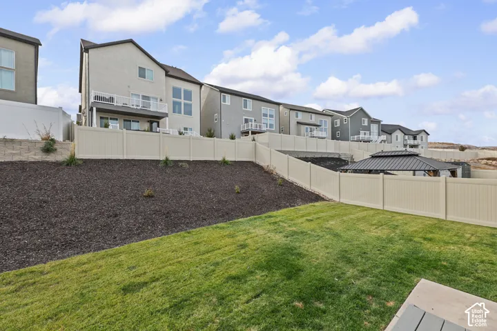 Rear exterior featuring a manicured lawn, tiered landscape bed, privacy fencing, and a built-in gazebo with a metal roof
