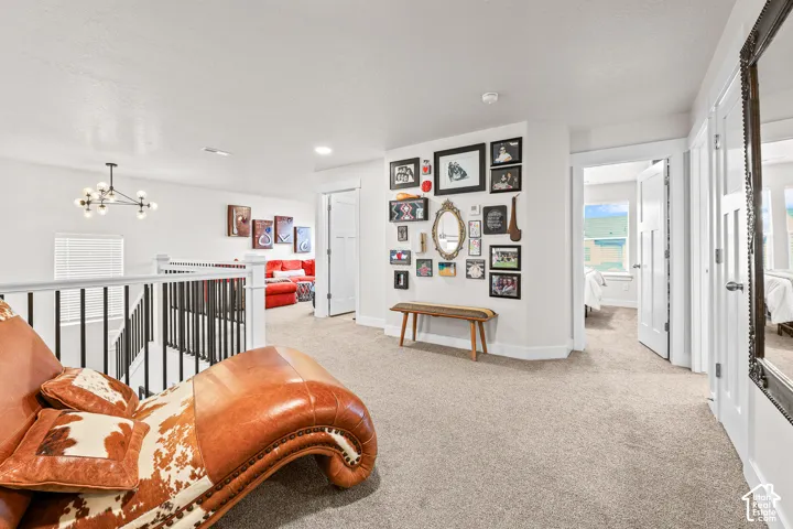 Neutral-toned interior featuring wall-to-wall carpeting, black metal spindle railing, multi-bulb modern chandelier, and multi-panel doors