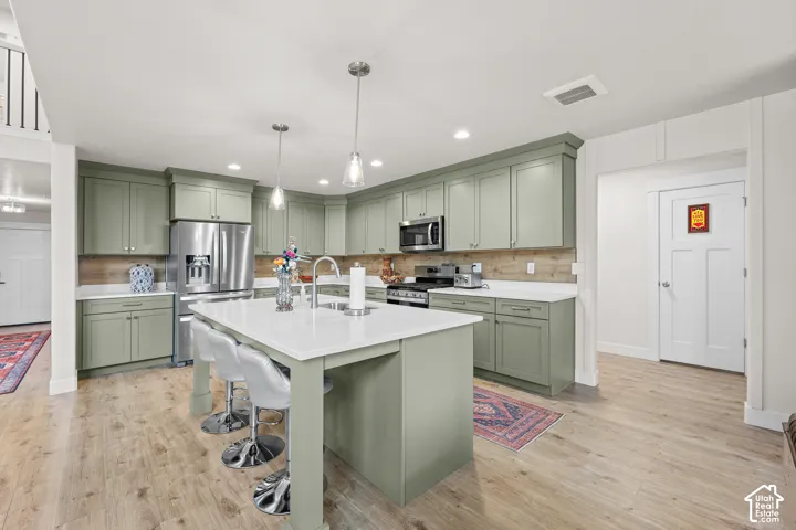 Kitchen featuring sage green cabinetry, a central island with a white countertop, wood-finish flooring, stainless steel appliances, and a wood-toned backsplash