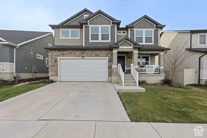 Two-story residence featuring a stone and vertical siding exterior, a covered front porch with white railing, and an attached two-car garage