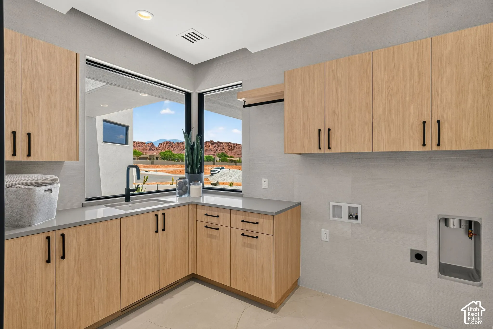 Light wood-finish cabinetry with matte black hardware, solid surface countertops, undermount sink with matte black faucet, and corner windows