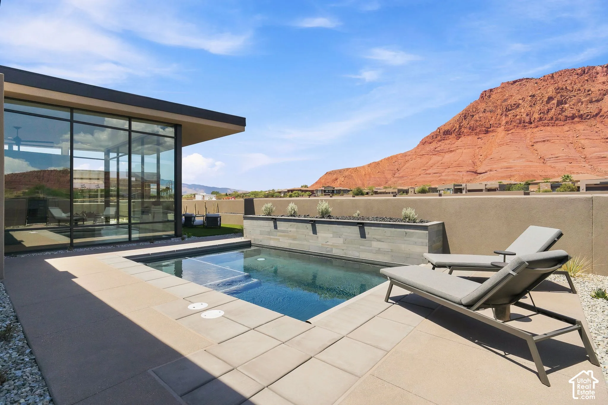 Outdoor area featuring a concrete-tiled patio, a rectangular swimming pool with integrated steps, and a stone-clad planter wall, set against a prominent mountain backdrop