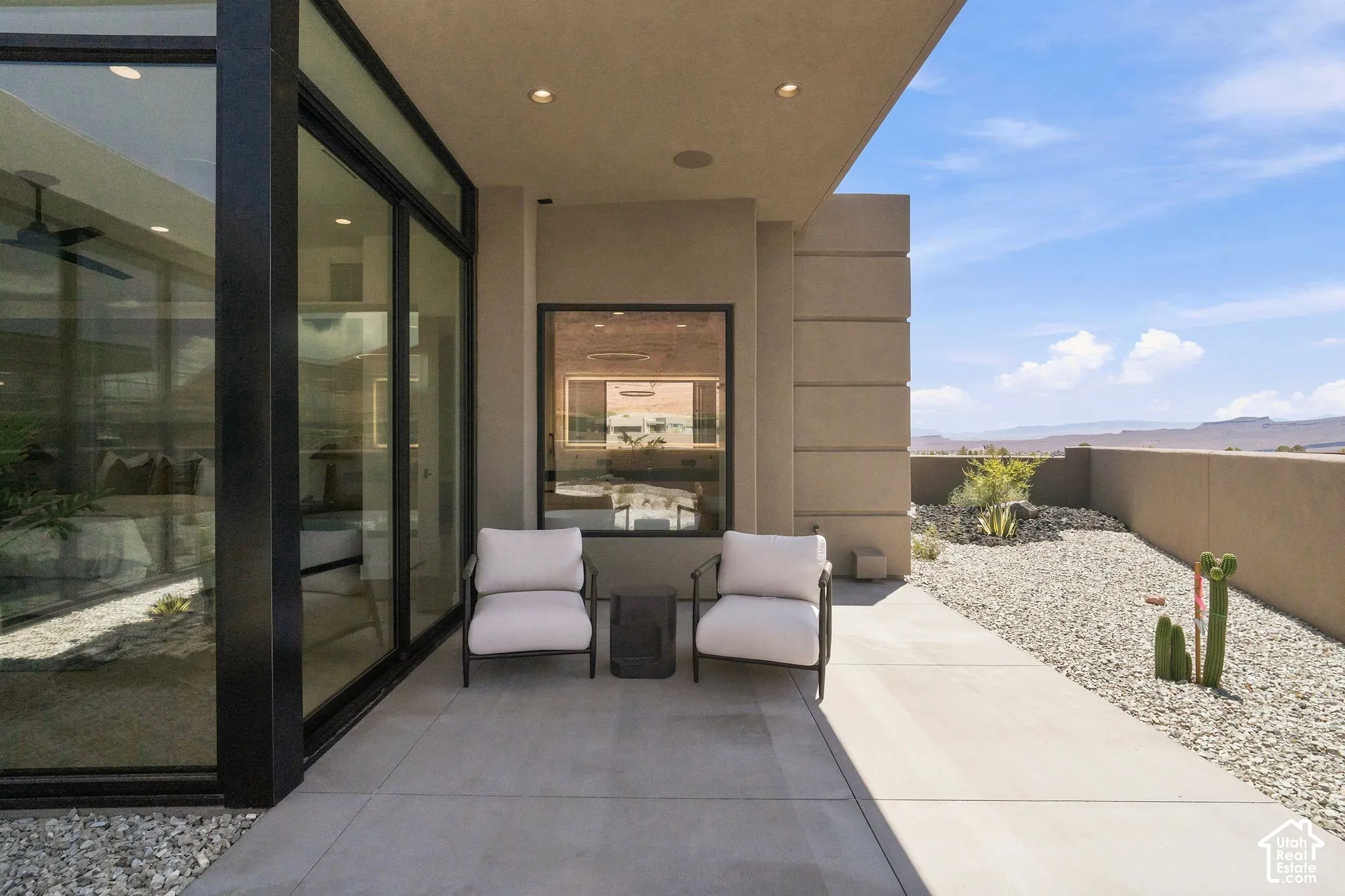 Covered patio featuring concrete flooring, floor-to-ceiling black-framed glass walls, recessed lighting, and xeriscaped rock landscaping