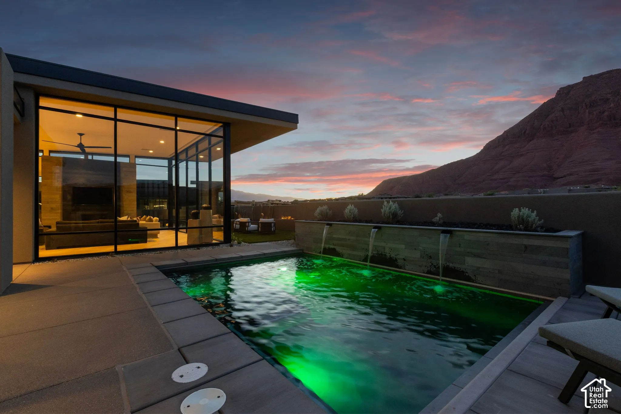 Modern exterior featuring floor-to-ceiling glass windows, a swimming pool with integrated water features, a tiered stone-finish retaining wall, and a concrete patio