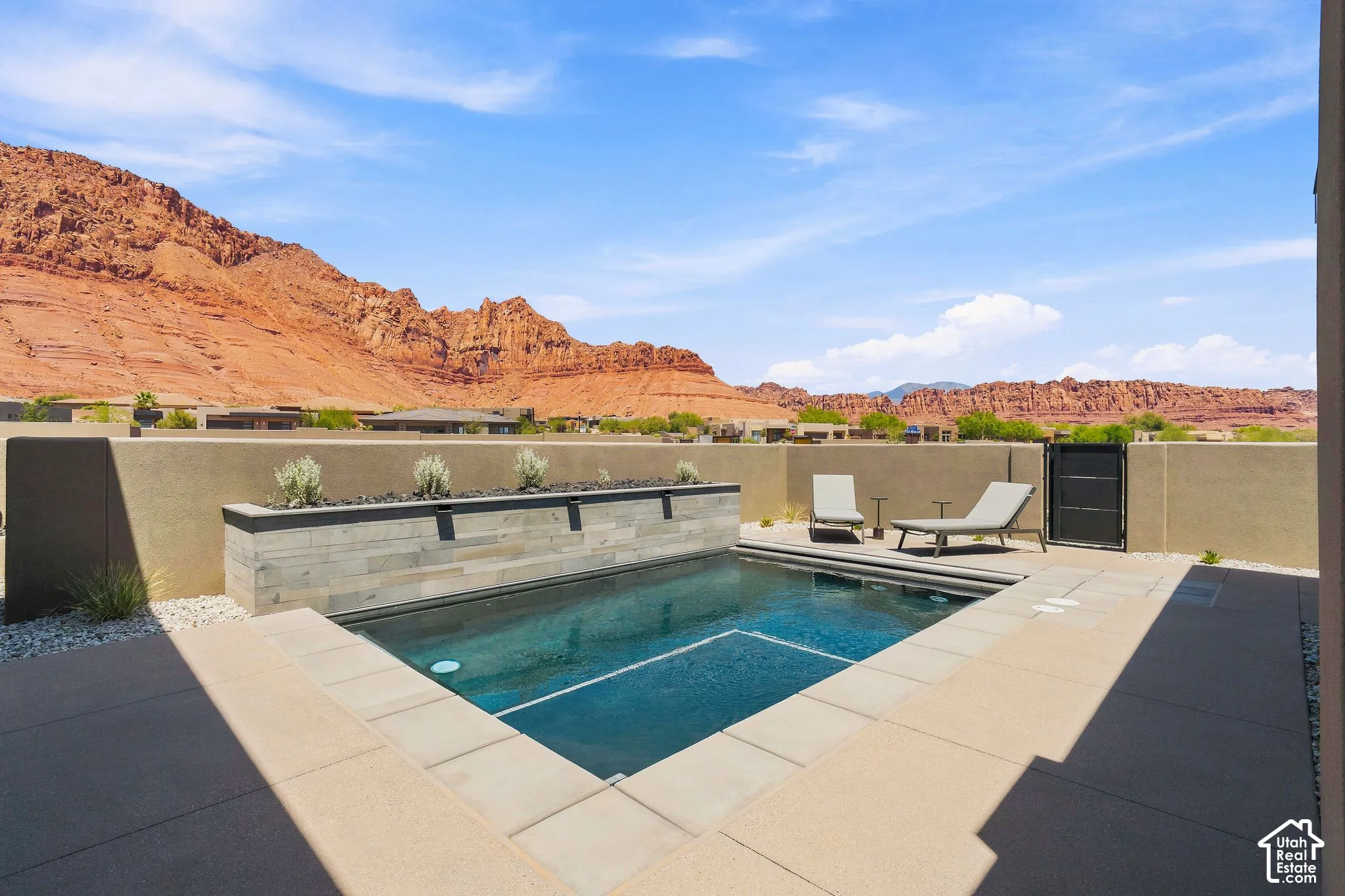 Private courtyard featuring a plunge pool, stone-clad water feature, concrete tile decking, and metal privacy wall, set against a mountainous backdrop