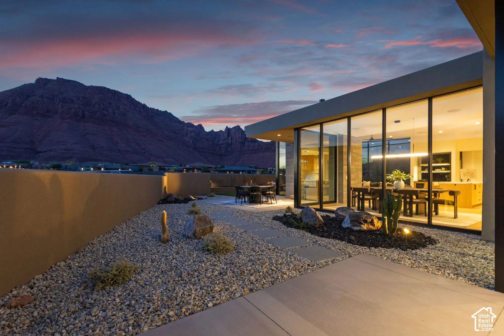 Modern outdoor patio featuring floor-to-ceiling glass walls, expansive mountain scenery, xeriscape landscaping with stone features, and concrete paver walkways