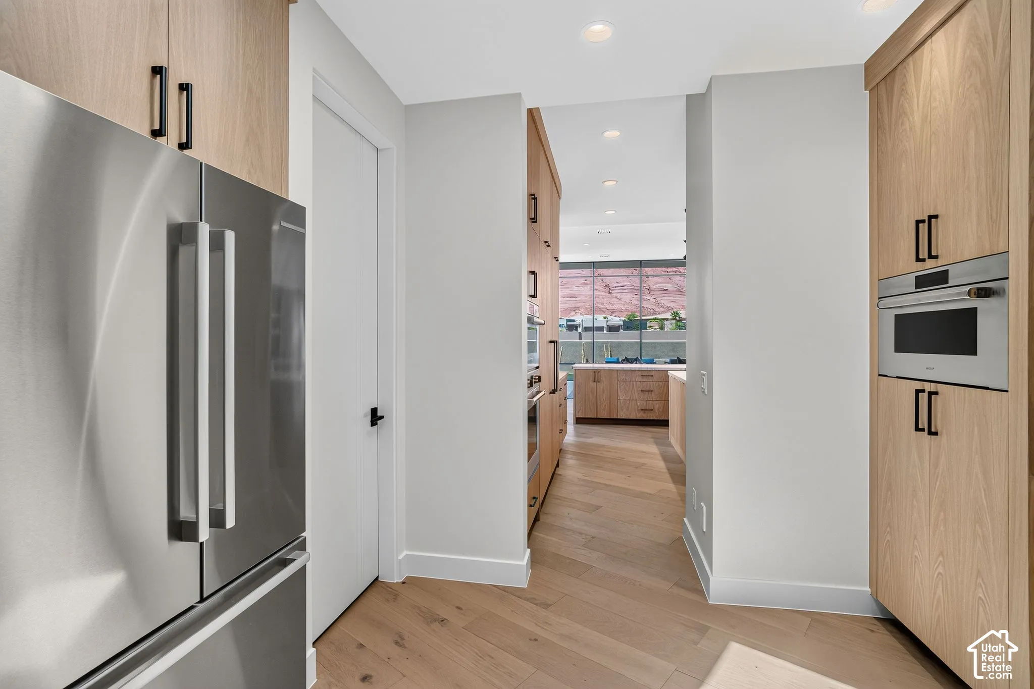 Custom flat-panel light wood cabinetry, stainless steel built-in appliances, matte black hardware, recessed lighting, and wood-finish flooring