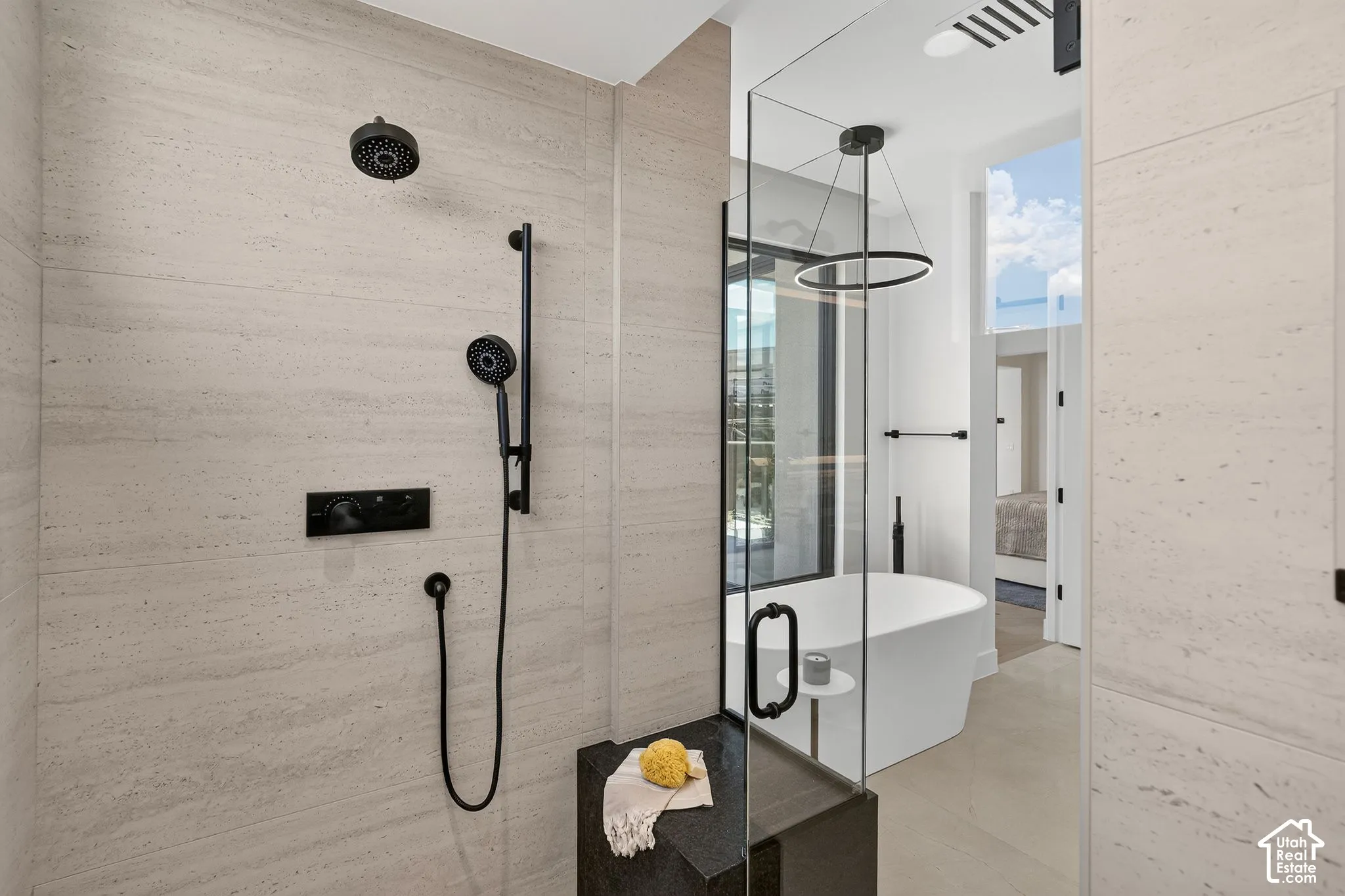 Walk-in shower featuring large-format stone-tile walls, matte black rainfall and handheld shower fixtures, and a built-in stone bench, paired with a freestanding soaking tub