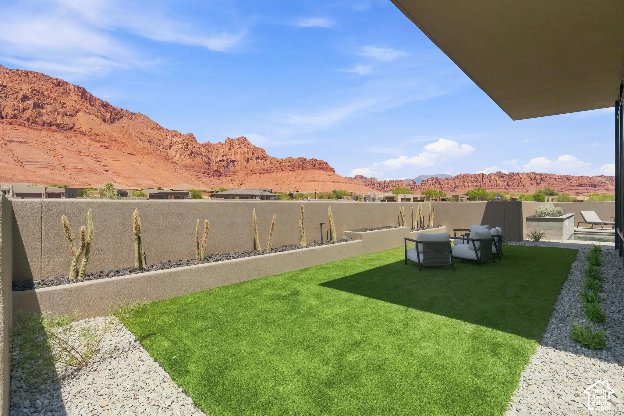 Patio featuring a covered area, synthetic turf, rock landscaping, tiered concrete walls, and natural sandstone mountain backdrop
