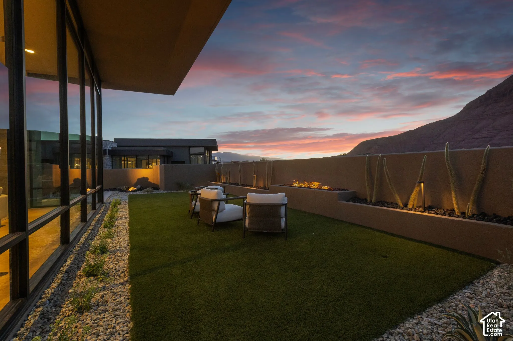 Outdoor courtyard featuring floor-to-ceiling glass paneling, artificial turf, low-profile masonry perimeter wall, built-in linear gas fireplace, and mountain backdrop
