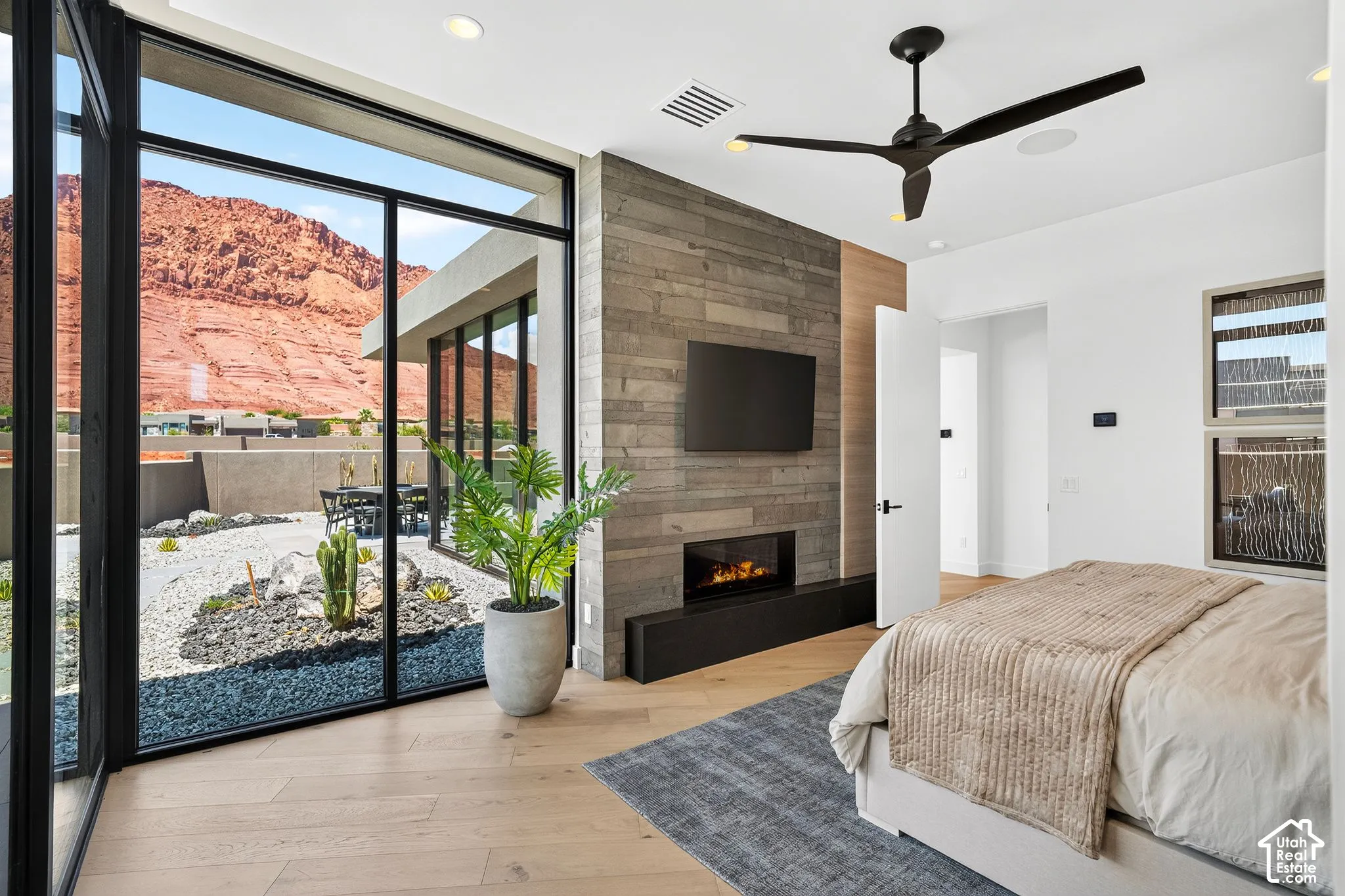 Floor-to-ceiling windows, wood-finish flooring, linear fireplace with a textured wood accent wall, and a ceiling fan