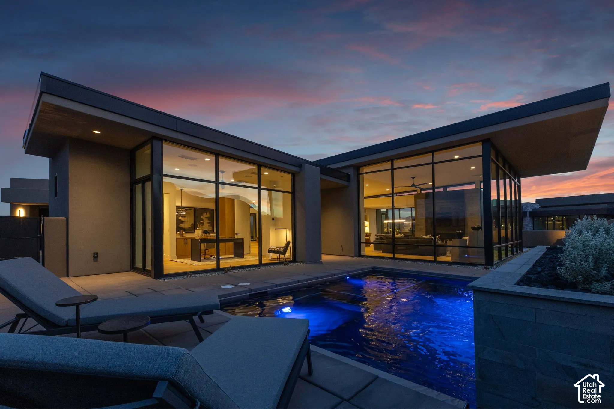 Modern architectural exterior featuring expansive floor-to-ceiling windows, deep roof overhangs, a private swimming pool, and stone-finished retaining walls