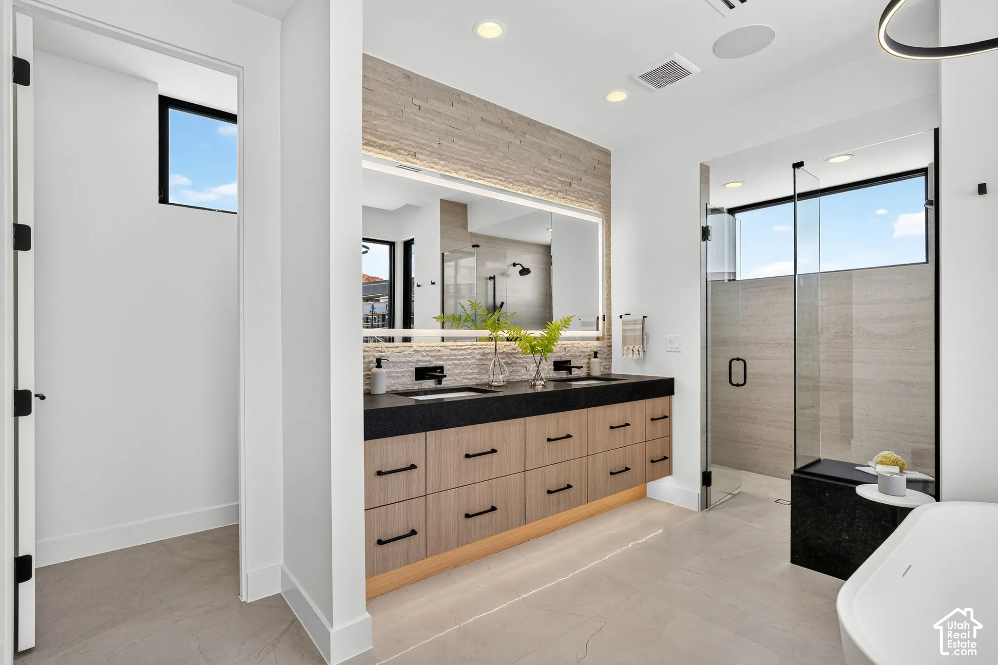 Floating double vanity with a dark countertop and wood-finish cabinetry, illuminated mirror with integrated backlighting, walk-in shower with a glass enclosure and bench, and a standalone tub