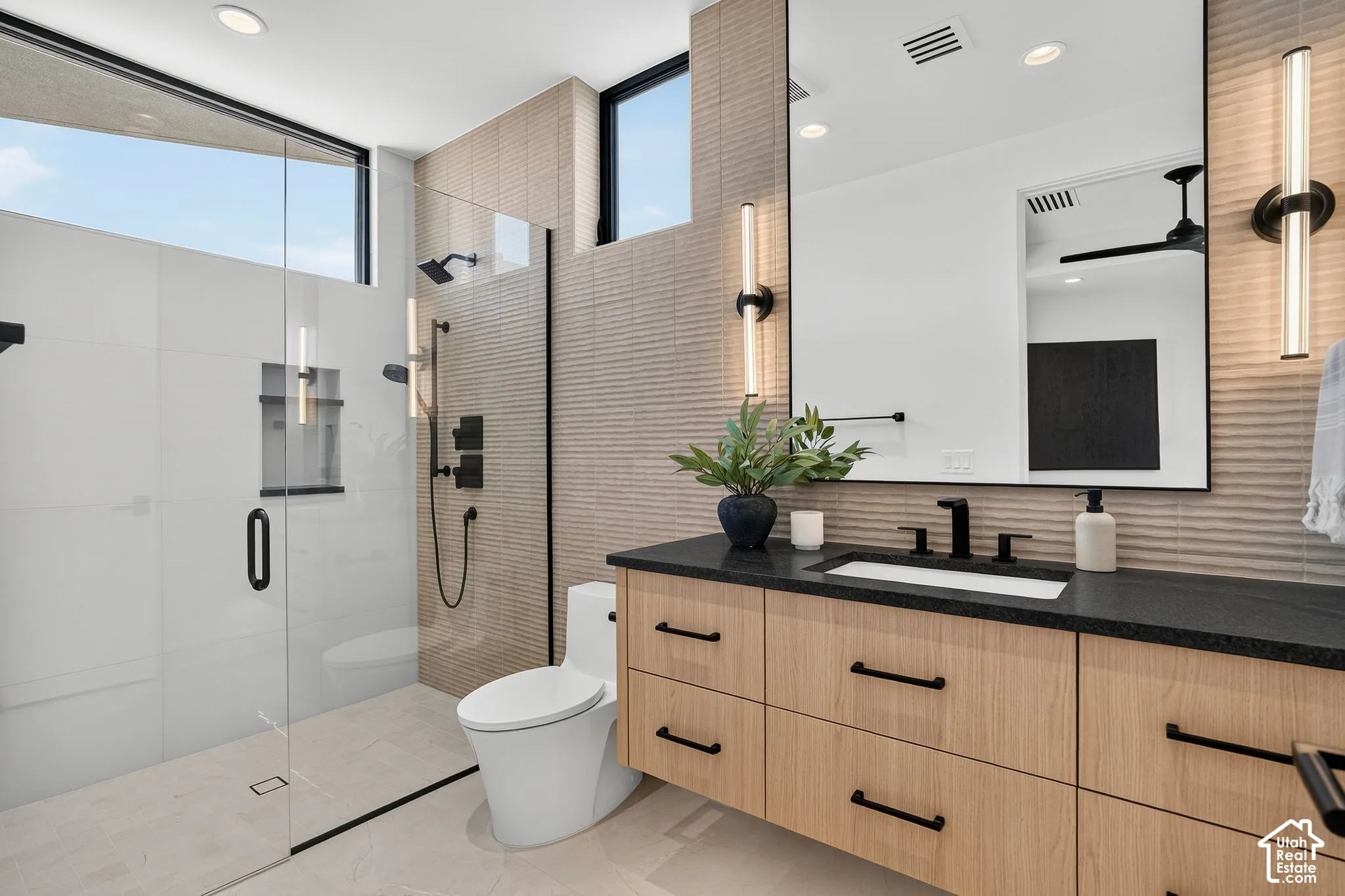 Floating vanity with wood-finish cabinetry, dark solid-surface countertop, rectangular undermount sink, matte black hardware, and textured wall tile