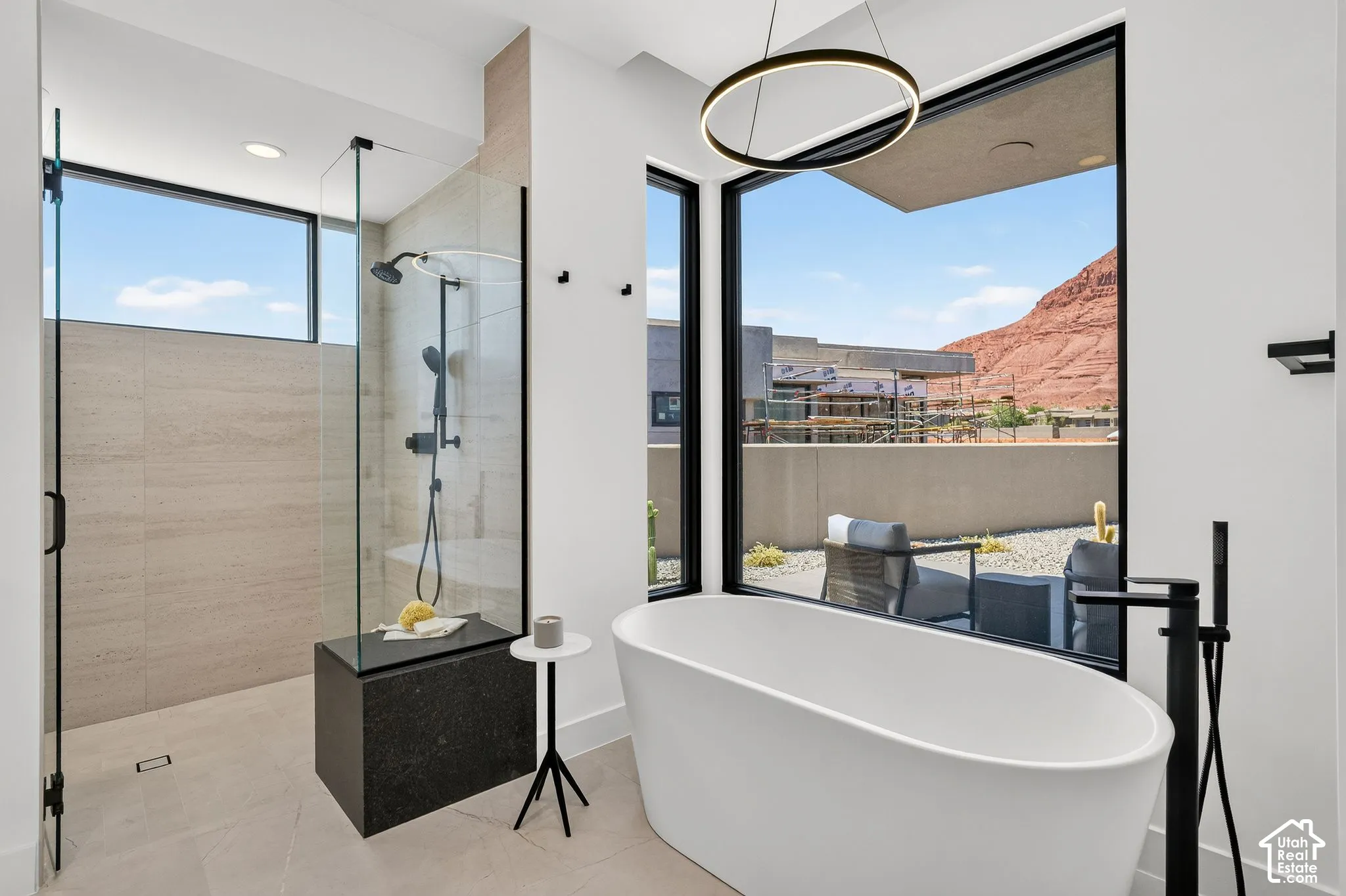 Walk-in shower with floor-to-ceiling tile, dark stone-finish bench, and glass enclosure, featuring a freestanding soaking tub, matte black plumbing fixtures, large-format window, and minimalist circular pendant lighting