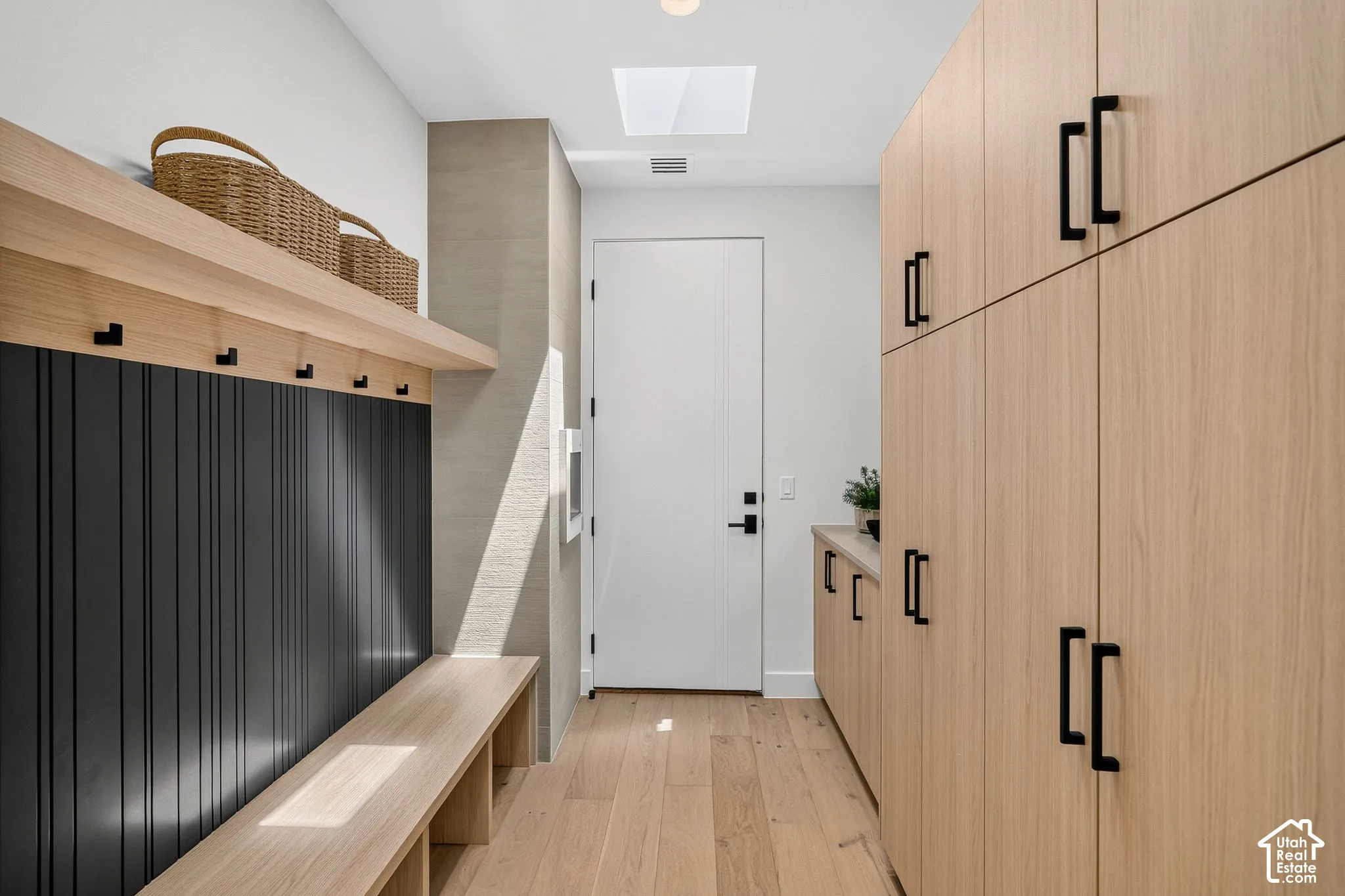 Custom wood-finish cabinetry, built-in bench seating, matte black hardware, vertical shiplap detailing, and a skylight