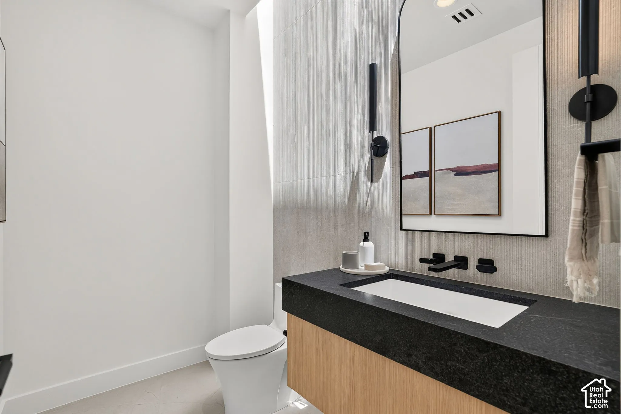 Floating vanity with a dark countertop and integrated rectangular basin, arched wall mirror, matte black wall-mounted faucet, and vertical wall sconces