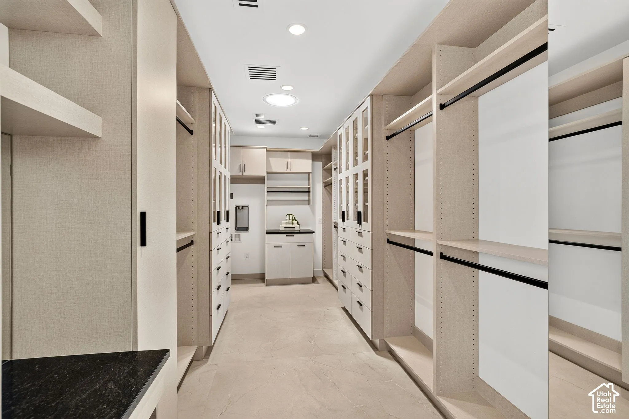 Custom built-in storage system featuring light wood-finish cabinetry, glass-front wardrobe doors, adjustable shelving, integrated garment rods, and dark stone-surface countertops