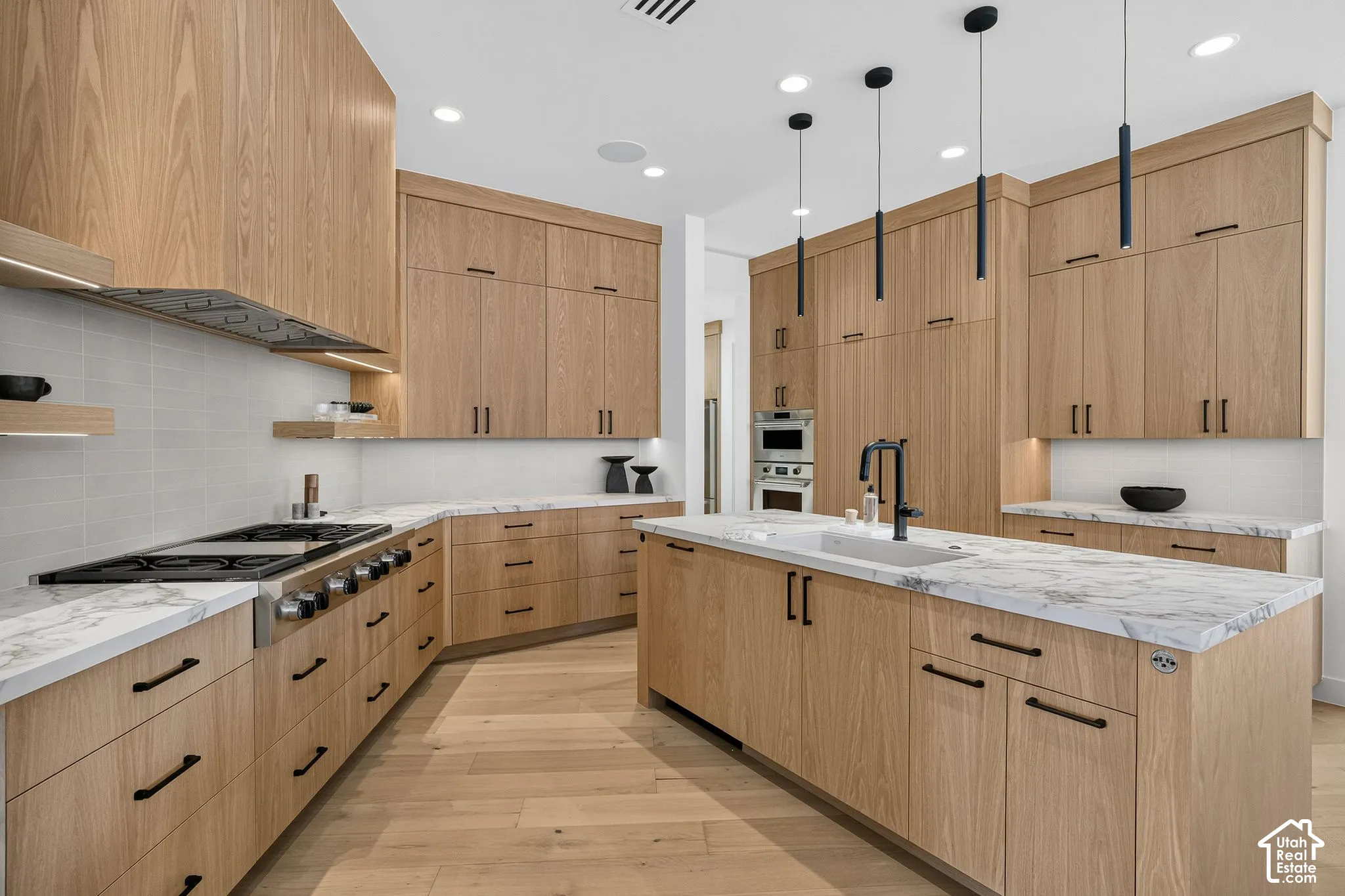 Kitchen featuring wood-finish cabinetry, stone-surface countertops, professional-grade gas range, central island with under-mount sink, and matte black pendant lighting