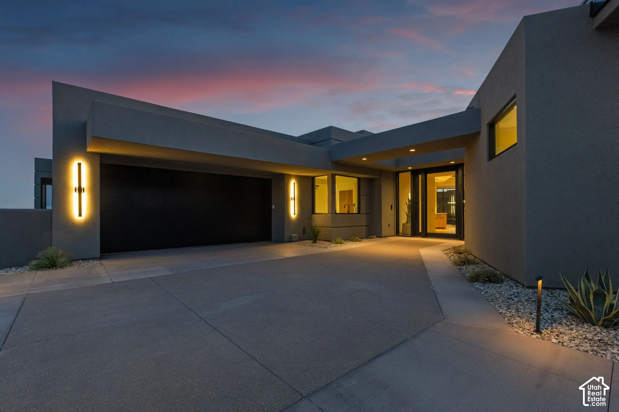 Modern architectural exterior featuring smooth stucco finish, recessed entry lighting, vertical wall-mounted fixtures, and a multi-car garage