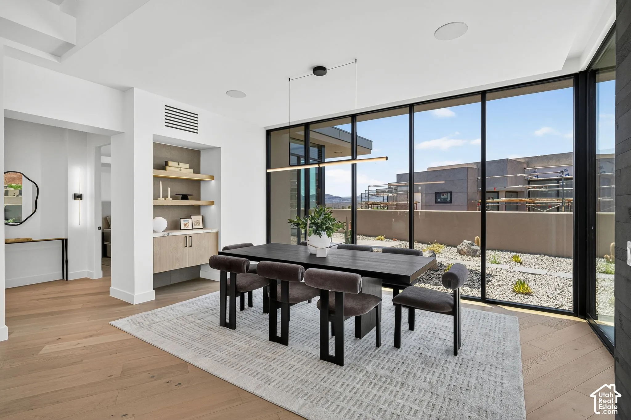 Floor-to-ceiling glass walls, wood-finish flooring, built-in cabinetry with integrated shelving, linear pendant lighting, and recessed ceiling speakers