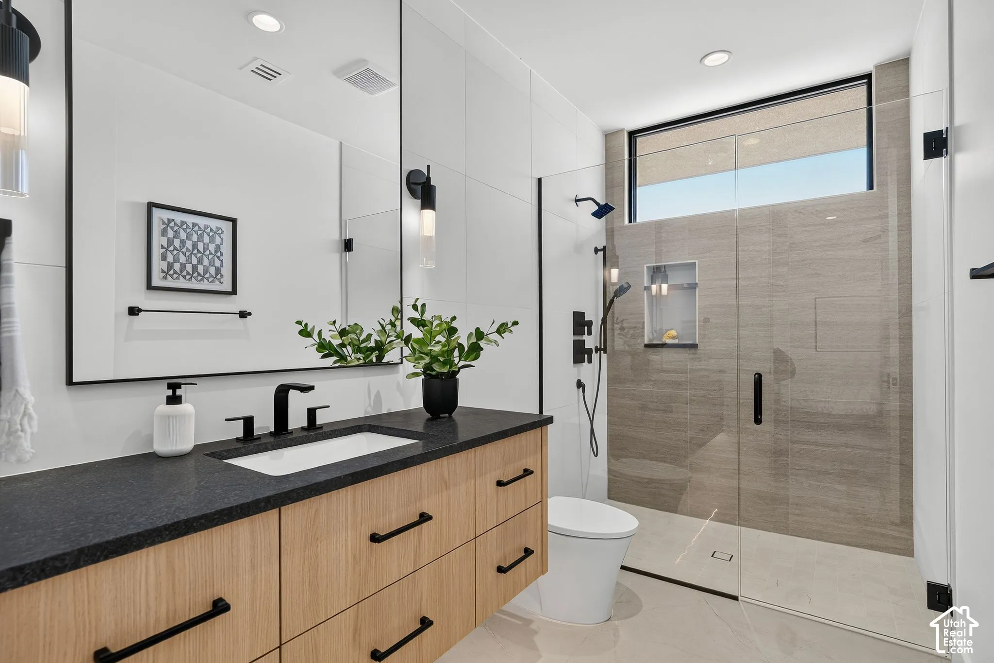 Floating wood-finish vanity with a dark countertop and undermount sink, large wall mirror, glass-enclosed walk-in shower with tile surround, built-in shower niche, and matte black hardware