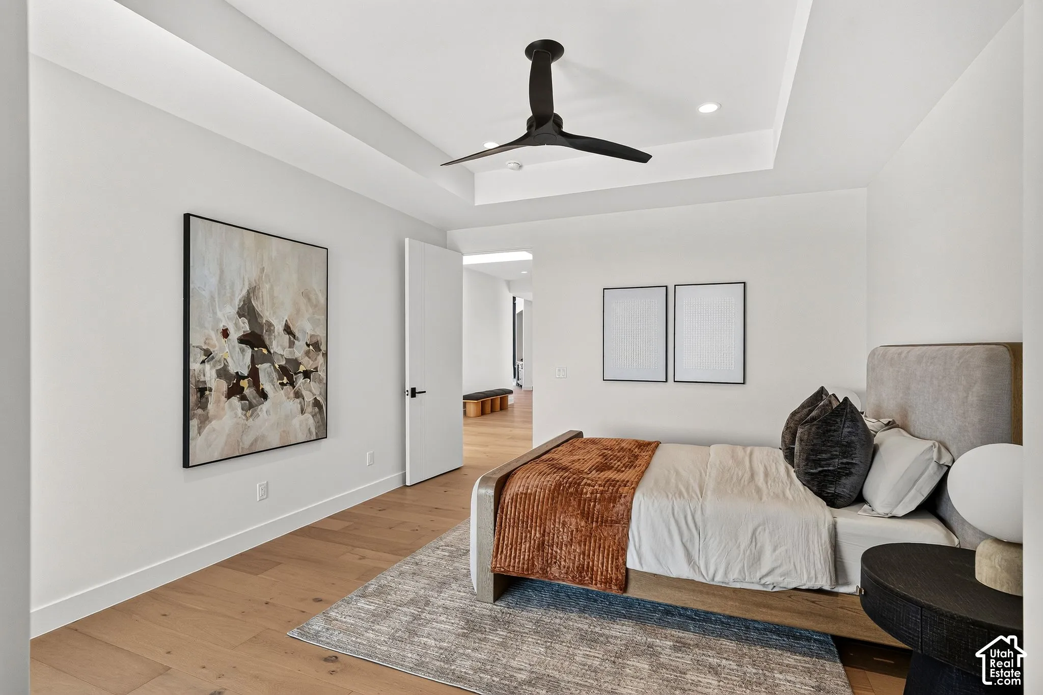 Tray ceiling featuring a recessed center, wood-finish flooring, and a matte black ceiling fan with recessed lighting