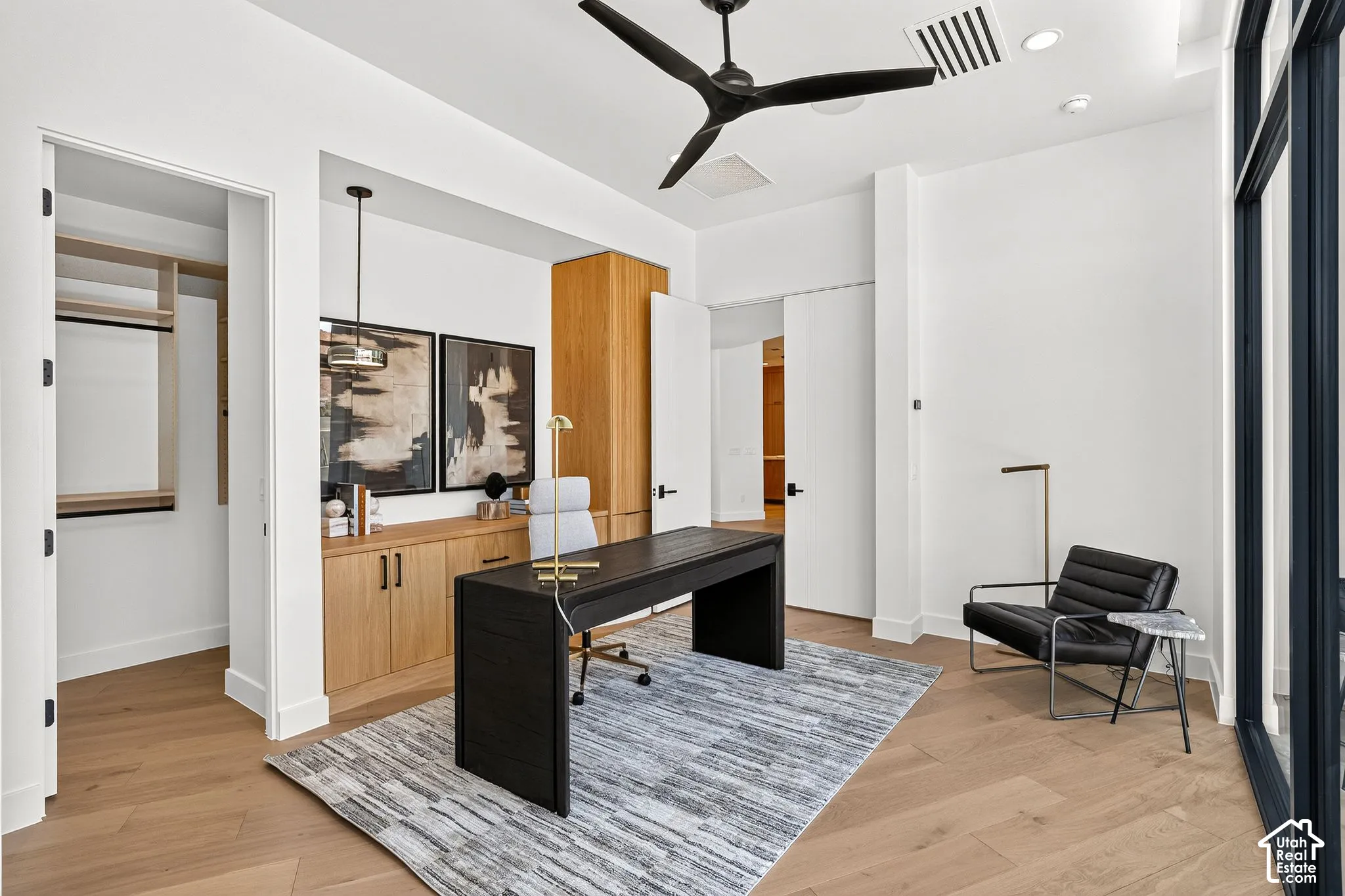 Custom built-in cabinetry with natural wood finish, wood-finish flooring, matte black three-blade ceiling fan, and black-framed glass-panel door