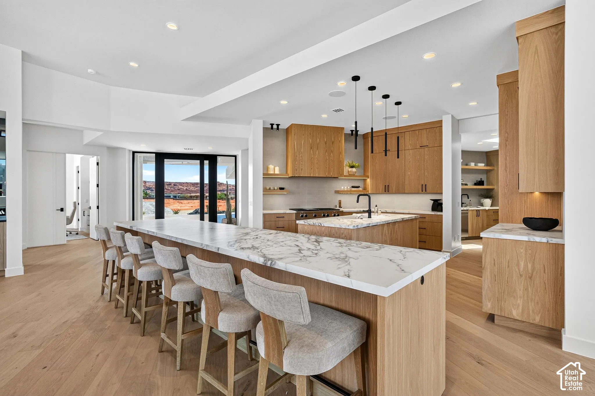Kitchen featuring custom light wood cabinetry, stone countertops with waterfall edge detailing, matte black hardware, recessed lighting, and wood-finish flooring