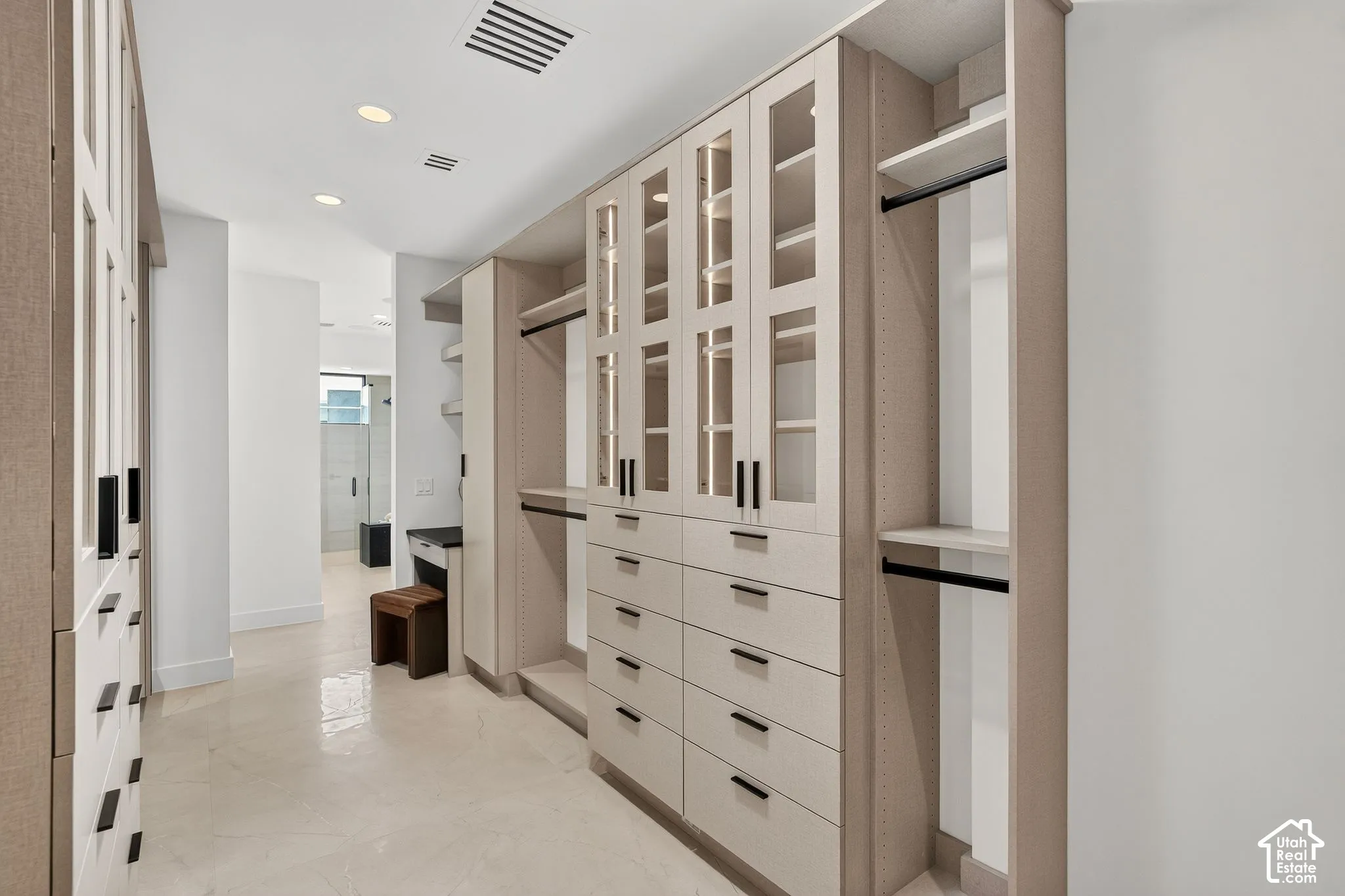 Custom walk-in cabinetry featuring glass-fronted upper doors, integrated lighting, matte black hardware, and an incorporated vanity station with polished stone surface