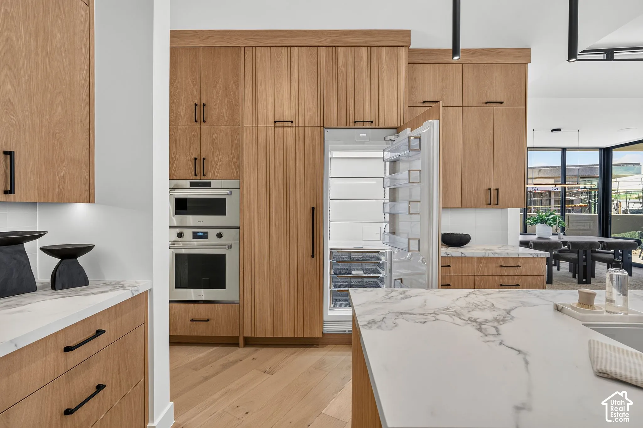 Modern kitchen featuring floor-to-ceiling wood cabinetry, panel-ready built-in refrigerator, integrated stainless steel double oven, stone-surface countertops with waterfall edge, and wood-finish flooring