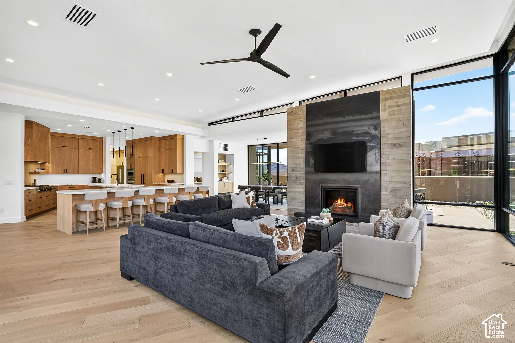Open-concept floor plan featuring wood-finish flooring, floor-to-ceiling windows, and a floor-to-ceiling stone fireplace surround with a metal accent panel