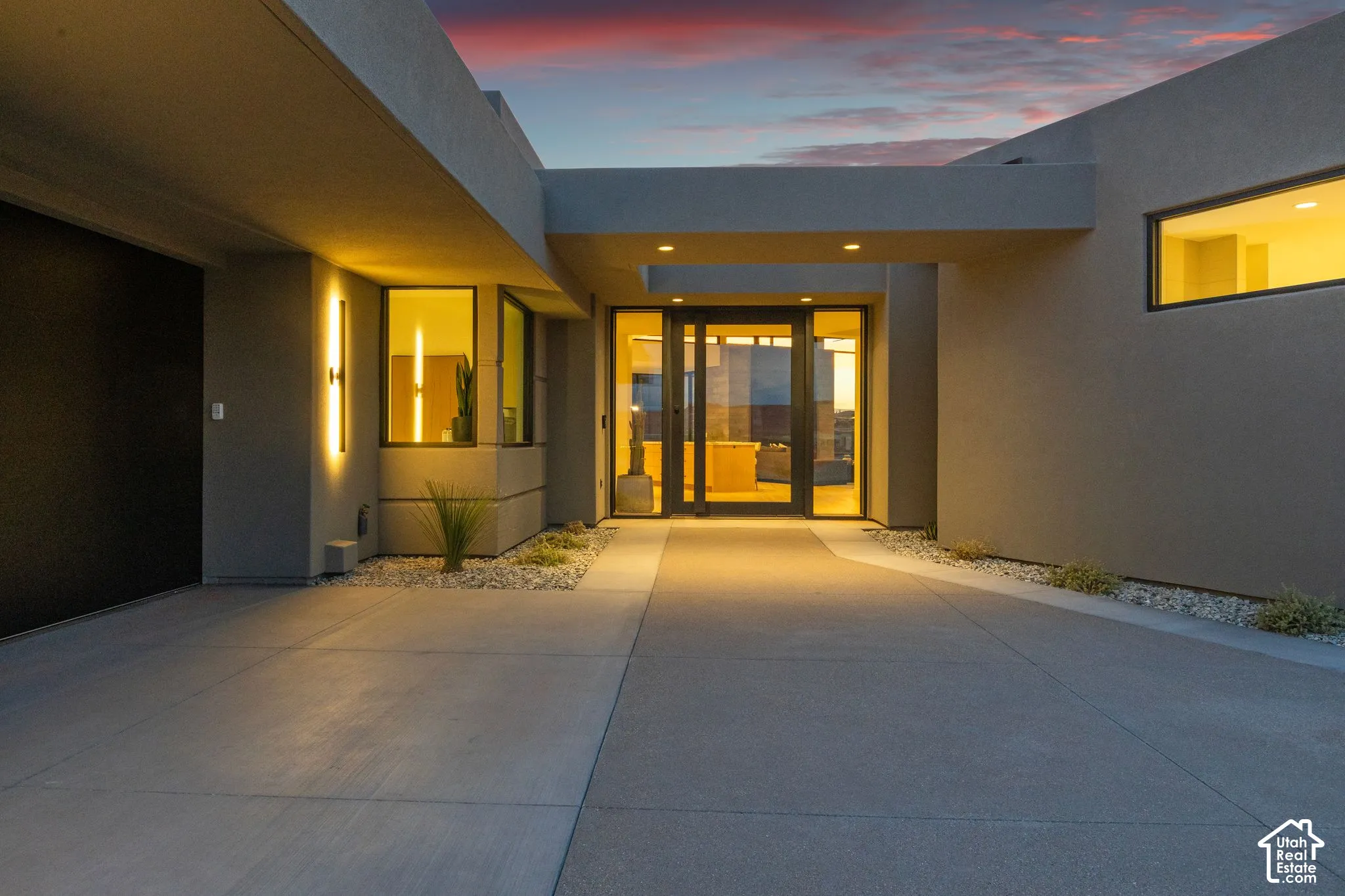 Contemporary exterior featuring a concrete entry path, smooth stucco facade, expansive glass-paned doorway, recessed ceiling lighting, and horizontal windows