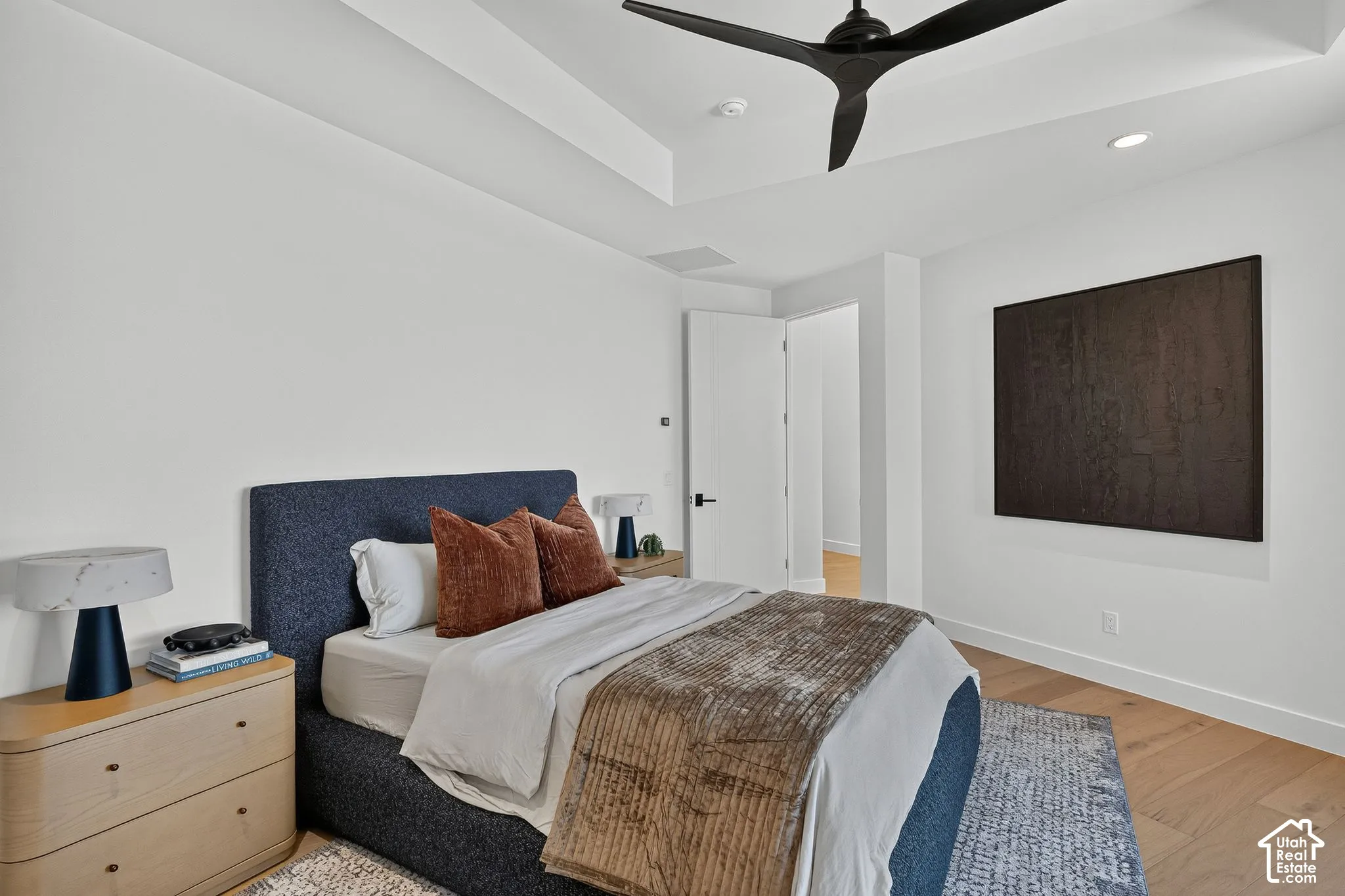 Tray ceiling featuring a contemporary matte black three-blade ceiling fan, light-toned wood-finish flooring, and crisp white walls