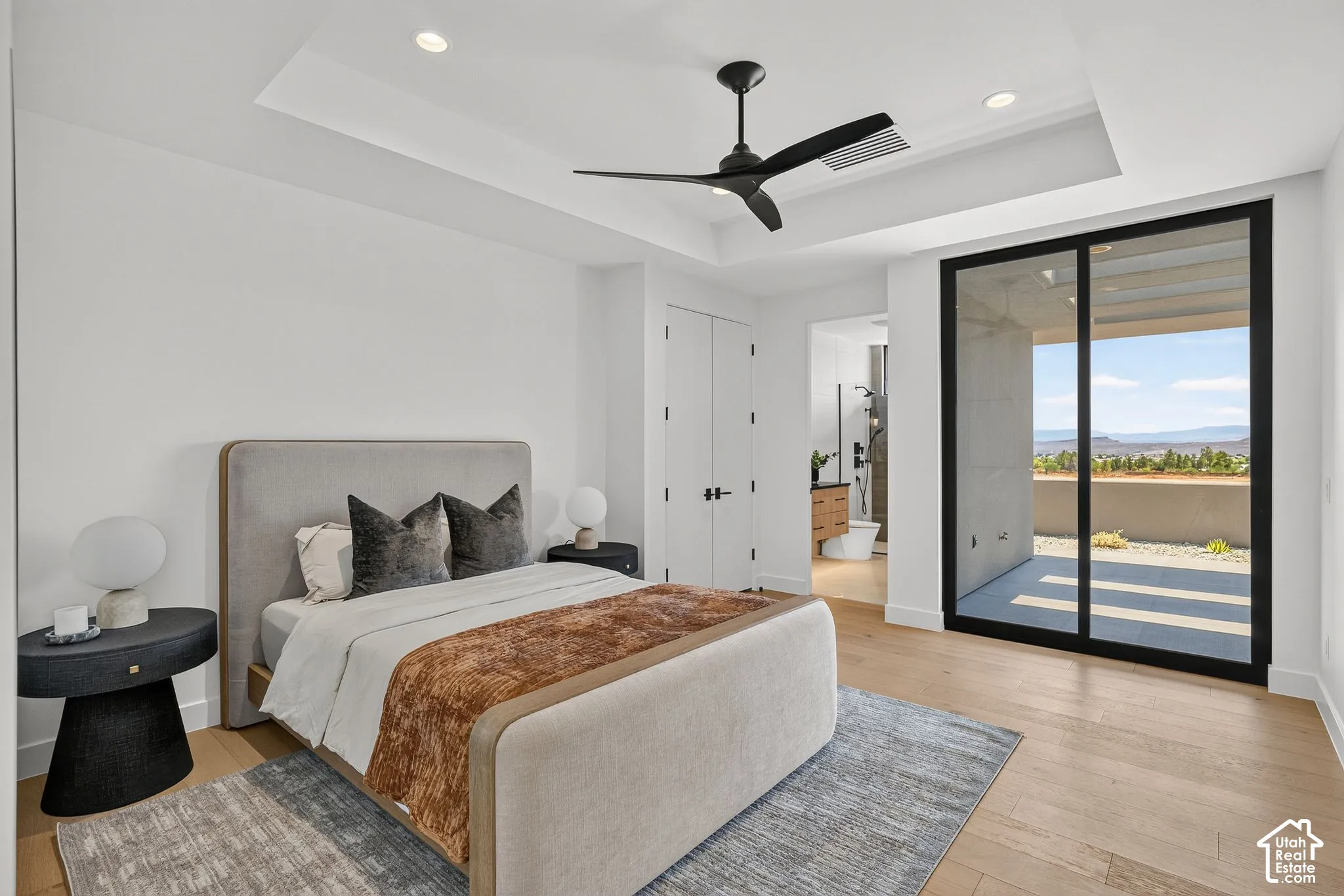 Bedroom featuring a tray ceiling with recessed lighting, matte black ceiling fan, wood-finish flooring, and a large sliding glass door providing external access