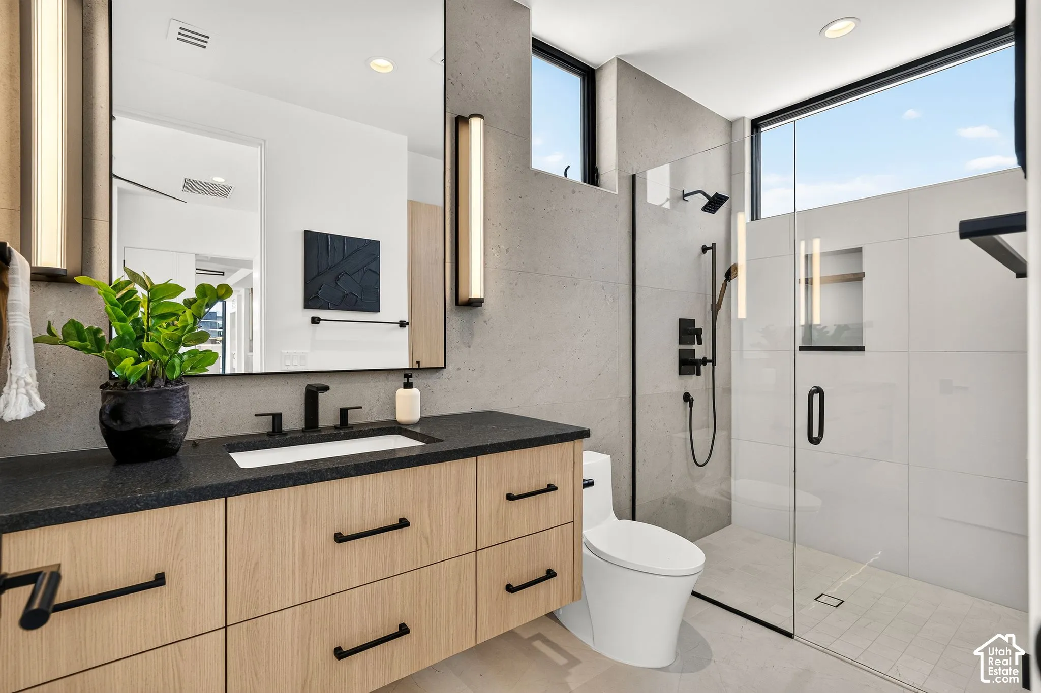 Floating light-wood vanity with a matte black faucet and dark countertop, large rectangular mirror, and a walk-in shower with matte black fixtures, glass enclosure, and built-in wall niche