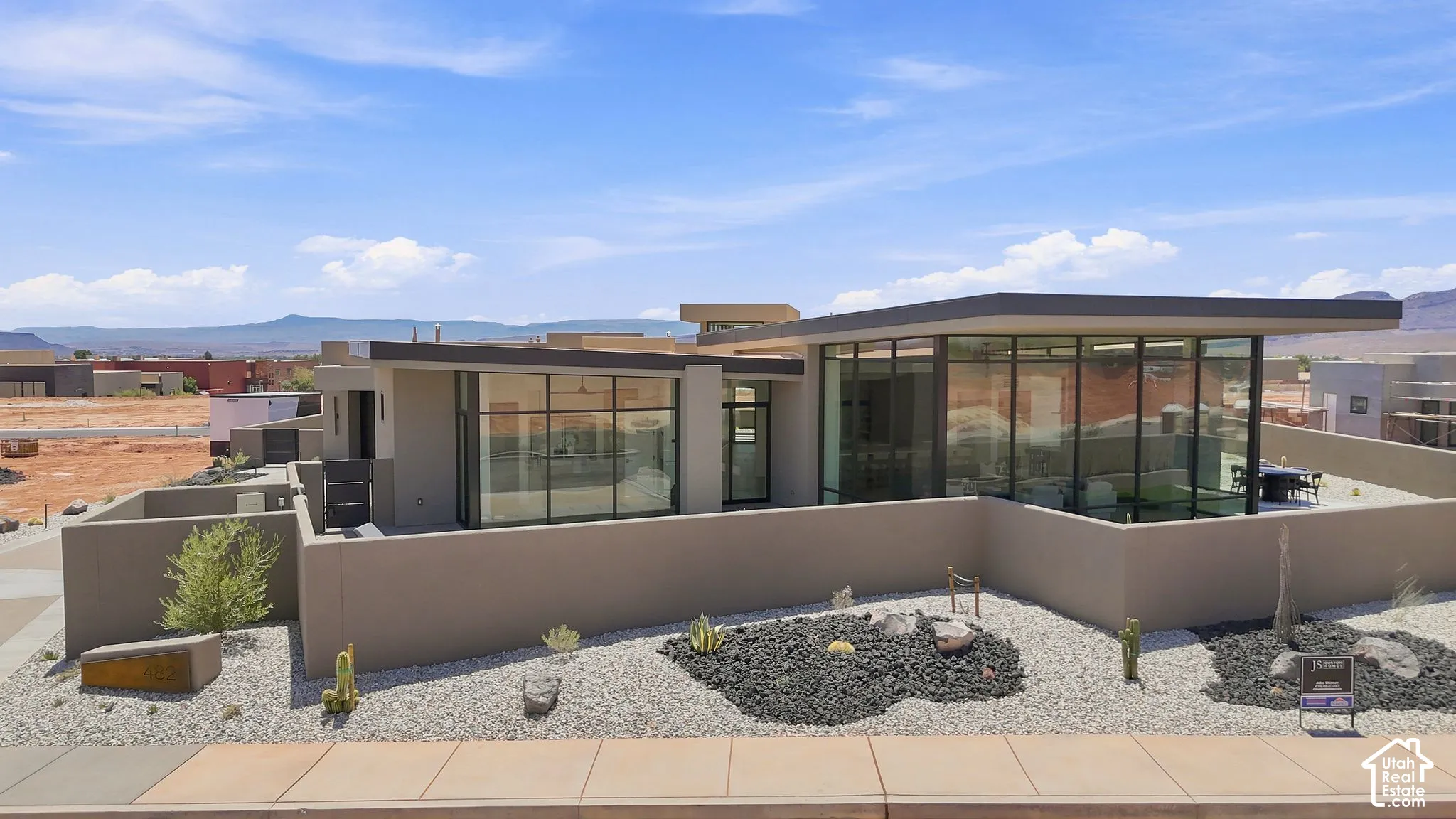 Contemporary desert residence featuring expansive floor-to-ceiling windows, flat roof architecture, stucco exterior siding, and a low-maintenance xeriscaped courtyard with natural stone accents