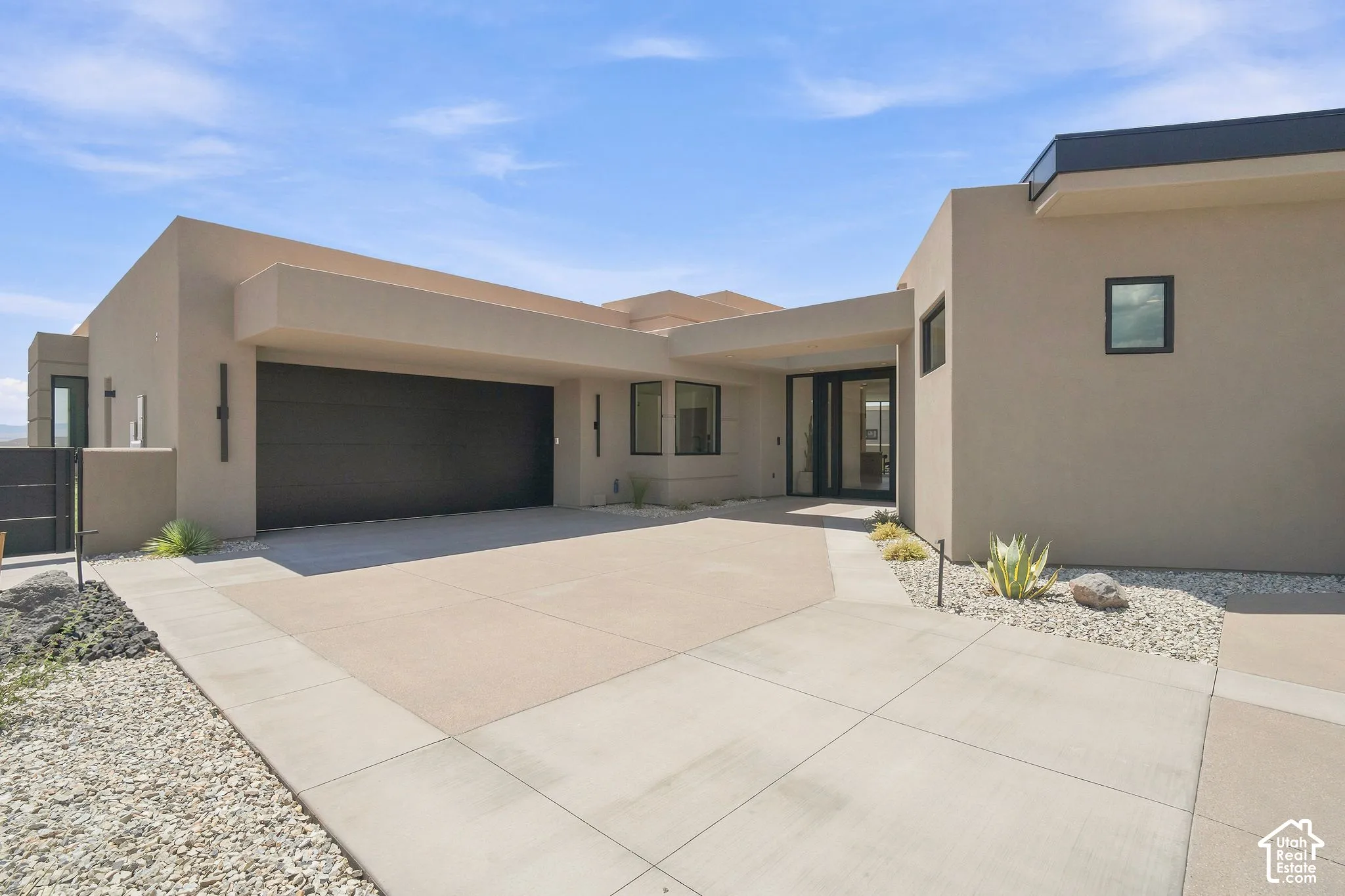 Modern stucco exterior featuring a flat roofline, integrated multi-car garage, recessed entryway, and professional desert xeriscaping